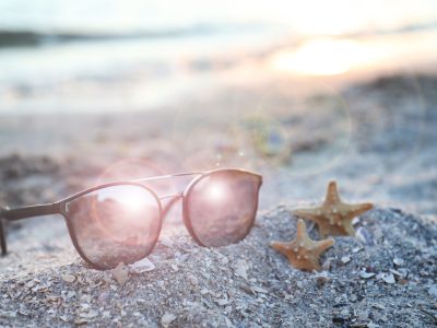 Stylish sunglasses and starfishes on sandy beach at sunset
